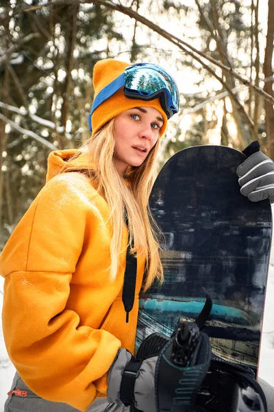 白人女性スノーボーダーは晴れた日に美しい雪の森の背景にスノーボードを保持しています. — ストック写真