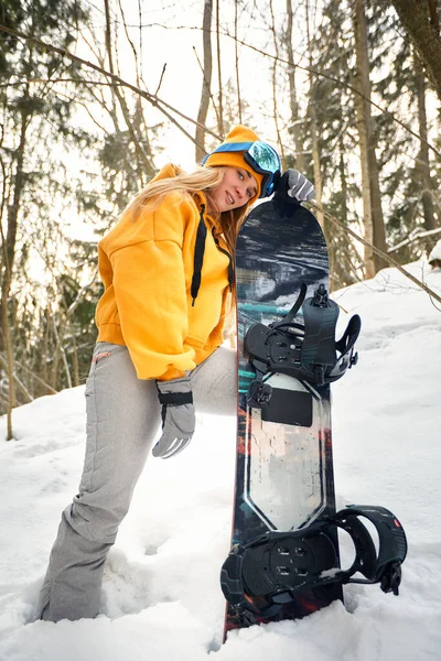 Junges Mädchen oder Snowboarderin geht zum Wintersport in verschneiten Wald sie steht im Schnee und hält ein Snowboard — Stockfoto