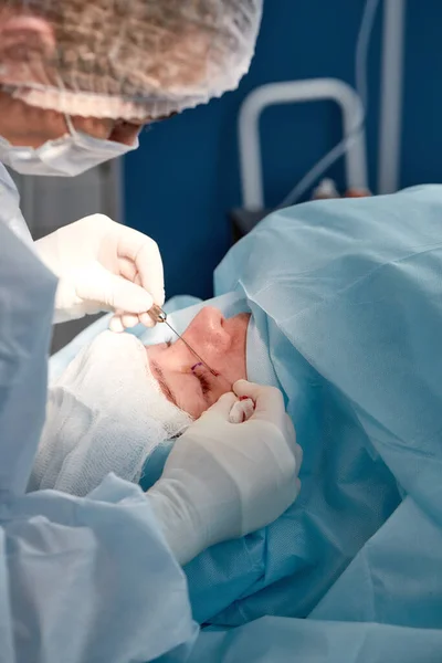Nahaufnahme des Gesichts eines Patienten, der sich einer Blepharoplastik unterzieht. Der Chirurg schneidet das Augenlid und führt Manipulationen mit medizinischen Instrumenten durch — Stockfoto