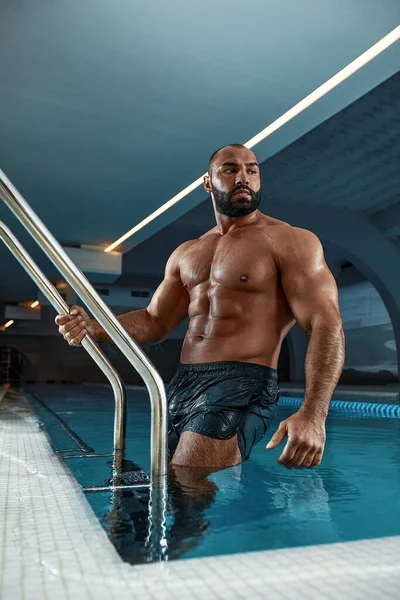 Retrato de um homem musculoso sexy molhado em pé na piscina — Fotografia de Stock