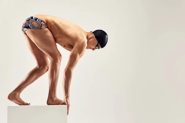 Hombre atlético joven listo para saltar a la piscina sobre fondo gris. El concepto de natación y juegos de agua. — Foto de Stock