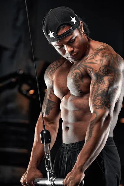 Homme à la peau foncée forte et musclée s'entraîne sur un équipement moderne dans la salle de gym. Portrait de musclé pompé entraîneur de conditionnement physique — Photo