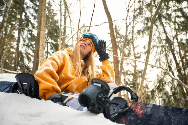 Caucasian woman snowboarder holds snowboard on beautiful snowy forest background in sunny day. — Stock Photo, Image