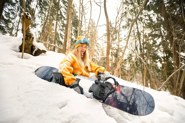 Mulher branca snowboarder detém snowboard no belo fundo da floresta nevada em dia ensolarado. — Fotografia de Stock