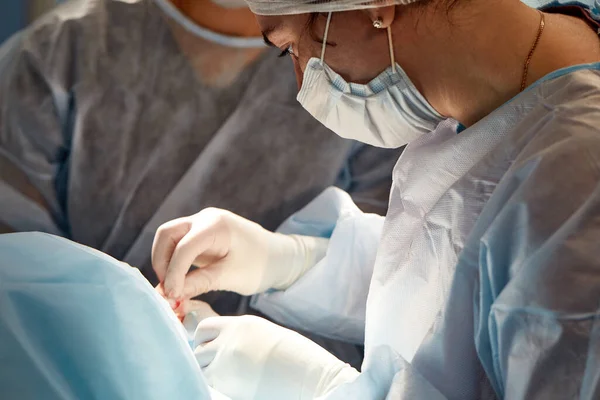 수술실에서 한 여성 외과의와 얼굴에 긴장된 표정을 짓고 있는 의사를 수술 방에서 자세히 관찰하고 있는 모습. — 스톡 사진