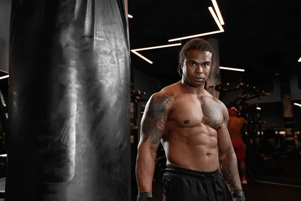 Ein Afroamerikaner trainiert im Fitnessstudio und faustet seine Boxsack-Fäuste. Konzept von: Fitness, Fitness, Boxen, Erfolg, Training und Power — Stockfoto