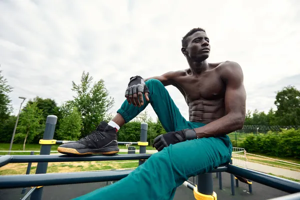 Guapo afroamericano deportista sentado en la calle mientras toma un descanso después del entrenamiento. Hombre negro descansando después del entrenamiento — Foto de Stock