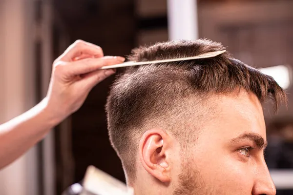 Хозяин стрижет волосы и бороду человека в парикмахерской, парикмахер делает стрижку для молодого человека. Концепция красоты, уход за собой. — стоковое фото