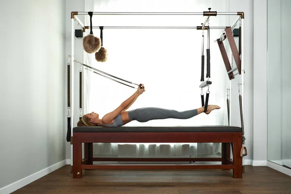 The instructor does exercises on the reformer, a beautiful girl trains on the modern reformer simulator to work out deep muscles, the modernized reformer equipment for Pilates and yoga. — Stock Photo, Image
