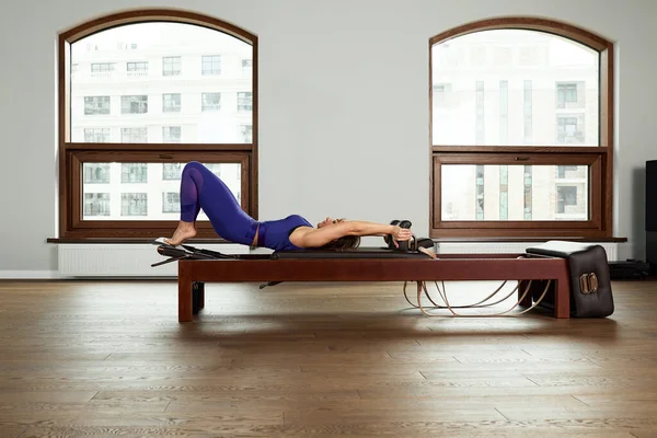 The instructor does exercises on the reformer, a beautiful girl trains on the modern reformer simulator to work out deep muscles, the modernized reformer equipment for Pilates and yoga. — Stock Photo, Image