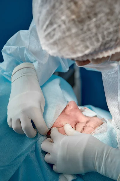 Närbild av ansiktet på en patient som genomgår blefaroplastik. Kirurgen skär ögonlocket och utför manipulationer med hjälp av medicinska instrument — Stockfoto