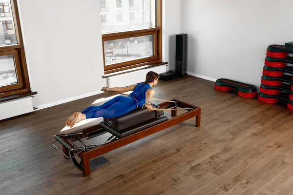 L'instructeur fait des exercices sur le réformateur, une belle fille s'entraîne sur le simulateur de réformateur moderne pour travailler les muscles profonds, l'équipement de réformateur modernisé pour Pilates et yoga. — Photo