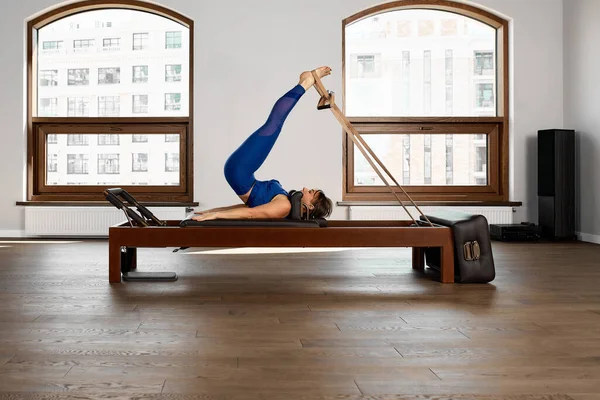 The instructor does exercises on the reformer, a beautiful girl trains on the modern reformer simulator to work out deep muscles, the modernized reformer equipment for Pilates and yoga. — Stock Photo, Image