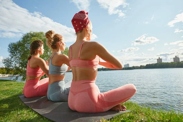 Three fit young beautiful women doing Reverse Warrior Pose, Crescent lunge variation, Viparita Virabhadrasana, working out in park on summer day, wearing sportswear tops, full length. Fitness, sport — Stock Photo, Image