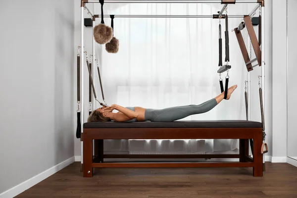 Beautiful girl trains on the modern reformer simulator to work out deep muscles, the modernized reformer equipment for Pilates and yoga. — Stock Photo, Image