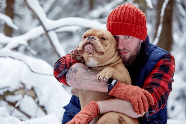 Hombre feliz sosteniendo un perro encantador en sus manos en el bosque nevado. Niño sonriente abrazando adorable cachorro en madera de invierno. Amante de mascotas. Perro - concepto de amigo humano. —  Fotos de Stock