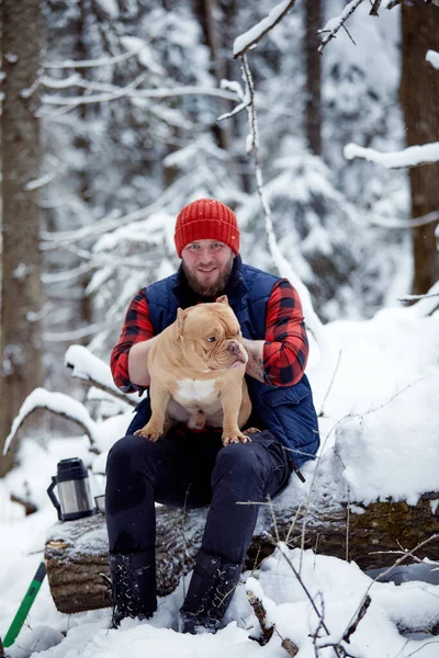 Hombre feliz sosteniendo un perro encantador en sus manos en el bosque nevado. Niño sonriente abrazando adorable cachorro en madera de invierno. Amante de mascotas. Perro - concepto de amigo humano. — Foto de Stock