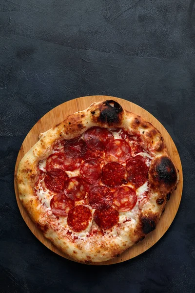 Lekkere pepperoni pizza en koken ingrediënten tomaten basilicum op zwarte beton achtergrond. Bovenaanzicht van hete pepperoni pizza. Met kopieerruimte voor tekst. Vlakke plaat. — Stockfoto