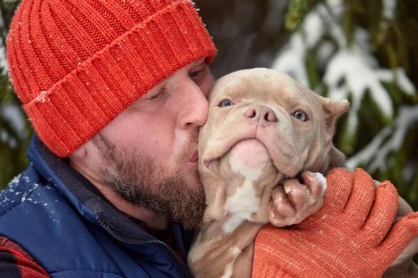 Homem feliz segurando cão adorável em suas mãos na floresta nevada. Garoto sorridente abraçando cachorrinho adorável em madeira de inverno. Amante de animais. Cão - conceito de amigo humano. — Fotografia de Stock