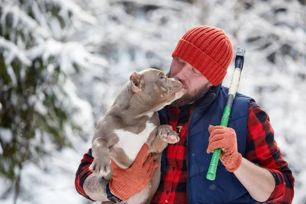 Happy man holding lovely dog in his hands in snowy forest. Smiling boy hugging adorable puppy in winter wood. Pet lover. Dog - human s friend concept. — Fotografia de Stock