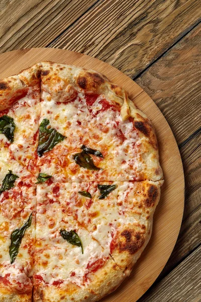 Pizza italienne non coupée servie avec une feuille de basilic fraîche sur un plateau en bois sur fond de texture sombre. Pizza piquante aux tomates et sauce pesto — Photo