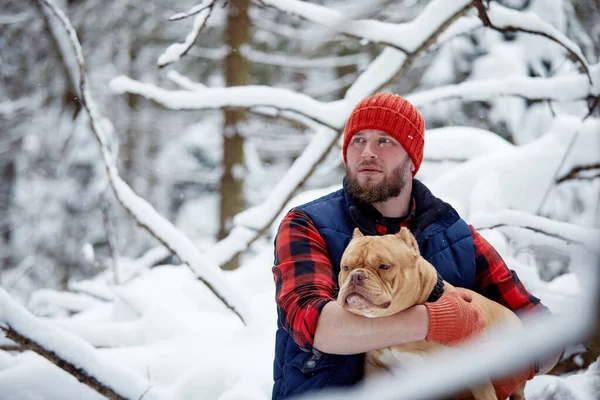 Hombre feliz sosteniendo un perro encantador en sus manos en el bosque nevado. Niño sonriente abrazando adorable cachorro en madera de invierno. Amante de mascotas. Perro - concepto de amigo humano. — Foto de Stock