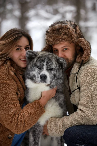 Casado joven pareja en un paseo en el bosque de invierno con una mascota perro husky —  Fotos de Stock