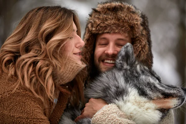 Retrato de um jovem belo casal de aparência europeia com um cão husky na floresta de inverno — Fotografia de Stock