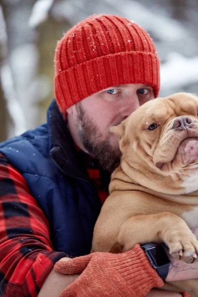 Hombre feliz sosteniendo un perro encantador en sus manos en el bosque nevado. Niño sonriente abrazando adorable cachorro en madera de invierno. Amante de mascotas. Perro - concepto de amigo humano. —  Fotos de Stock