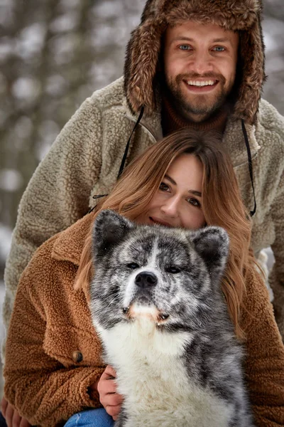 Pareja joven sonriendo y divirtiéndose en el parque de invierno con su perro husky —  Fotos de Stock