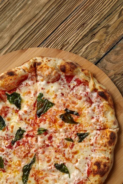 Ungeschnittene italienische Pizza mit frischem Basilikumblatt auf Holzbrett auf dunklem Hintergrund. Heiße Pizza mit Tomaten und Pesto-Sauce — Stockfoto
