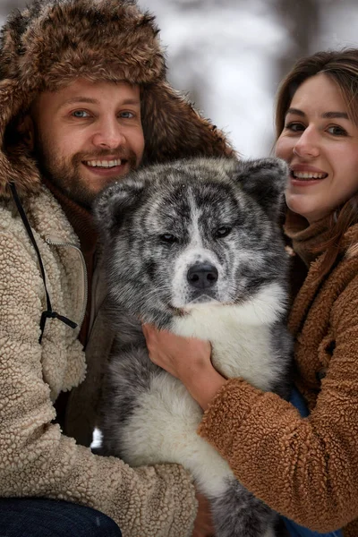 Pareja joven sonriendo y divirtiéndose en el parque de invierno con su perro husky —  Fotos de Stock