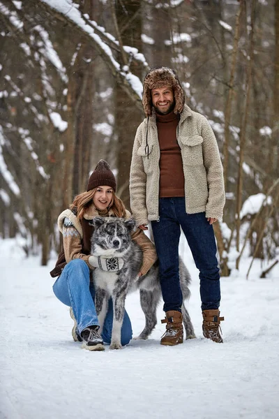 Retrato de um jovem belo casal de aparência europeia com um cão husky na floresta de inverno — Fotografia de Stock