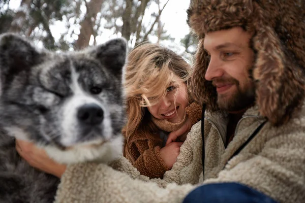 Feliz jovem casal em winterwear brincando com pura siberiana husky e se divertindo na floresta de pinheiros com neve — Fotografia de Stock