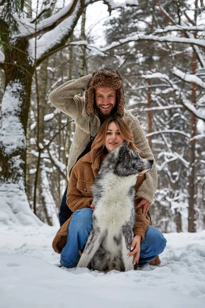 Jovem casal sorrindo e se divertindo no parque de inverno com seu cão husky — Fotografia de Stock