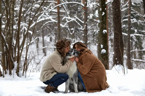 Retrato de um jovem belo casal de aparência europeia com um cão husky na floresta de inverno — Fotografia de Stock