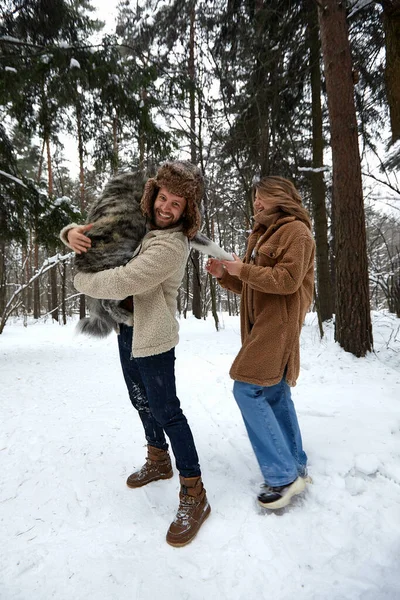 Retrato de una joven pareja hermosa de apariencia europea con un perro husky en el bosque de invierno — Foto de Stock