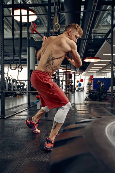 男子健身训练与大和重轮胎击中锤子。概念锻炼，交叉力量 — 图库照片