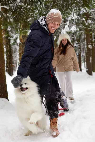 Família de mãe, pai e filho se divertindo em madeira de inverno nevado com cão de estimação cheerfull. — Fotografia de Stock