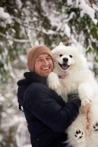 Um humano e um cão são os melhores amigos. Homem e cão caminham na floresta nevada no inverno na neve profunda em um dia ensolarado. — Fotografia de Stock