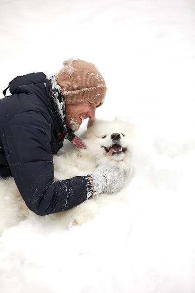 Um humano e um cão são os melhores amigos. Homem e cão caminham na floresta nevada no inverno na neve profunda em um dia ensolarado. — Fotografia de Stock