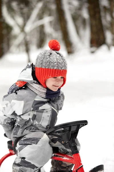 Glücklicher Junge im Winter mit dem Schlitten bergab. ein Kind in heller Kleidung sitzt auf einem Schlitten, Schnee fliegt ihm entgegen. — Stockfoto
