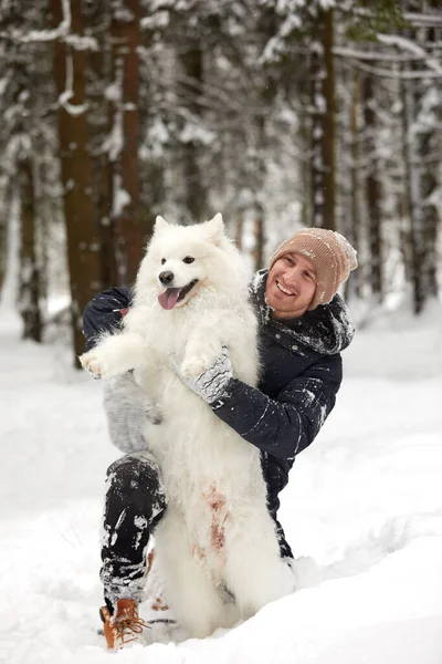 Um humano e um cão são os melhores amigos. Homem e cão caminham na floresta nevada no inverno na neve profunda em um dia ensolarado. — Fotografia de Stock