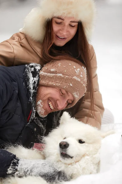 Feliz jovem casal em winterwear brincando com pura siberiana husky e se divertindo na floresta de pinheiros com neve — Fotografia de Stock