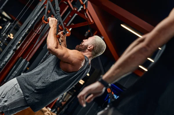 Ein Mann trainiert seine Arme und Brust im Fitnessstudio am Simulator, macht Übungen für verschiedene Muskelgruppen. Findet Motivation, sportlichen Lebensstil, Gesundheit, athletischen Körper, Körper positiv. Filmkorn. — Stockfoto