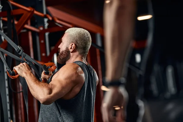 一个男人在体育馆里用模拟器锻炼他的胳膊和胸部，为不同的肌肉群做运动。发现动机，运动生活方式，健康，运动身体，身体积极。薄膜颗粒. — 图库照片