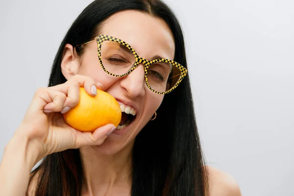 young woman in modern glasses bites lemon, raw fresh yellow citrus fruit, female happy smile, isolated on white background natural organic food concept.