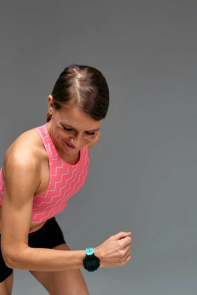 Determined muscular female athlete workout, raising leg and doing stretching exercises. Sport woman in sportswear training indoors, doing fitness aerobics, gray background