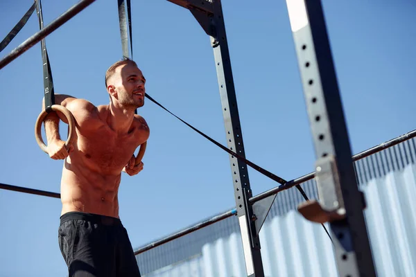 Muscular sportsman exercising on outdoor gymnastic rings in outdoor gym. Hands at rings dipping man doing exercise using rings.