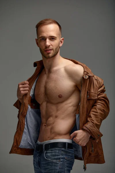 An attractive white man in jeans and black shirts tands in full growth against a gray background. Copy space.